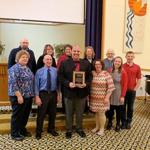 An image of Phil Maxwell with his award surrounded by family members.