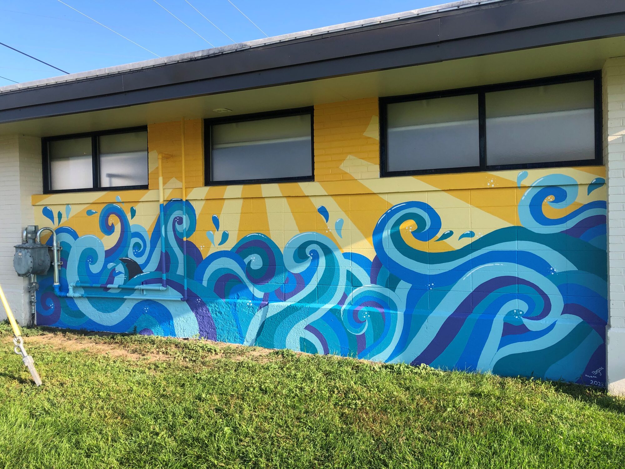 An image of the final mural which has a brightly colored sun with rays of light at the top and cheerful multihued blue waves and droplets of water on the lower half.