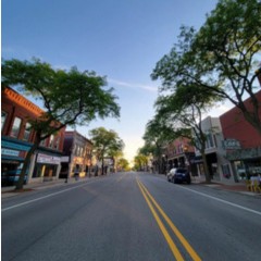 Quiet town street with trees and shops.